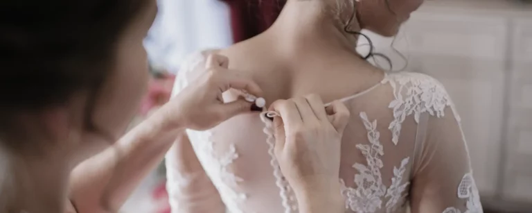 Tienda - Primer plano de la espalda de una mujer con un vestido de novia, una modista abrocha los botones del vestido por la espalda